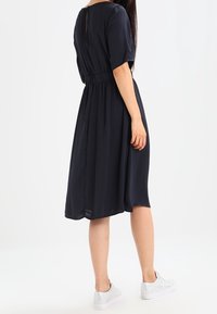 Mörkblå midi-klänning med korta ärmar, insvängd midja, mjukt tyg och en nyckelhålslösning på ryggen. Parat med vita sneakers.