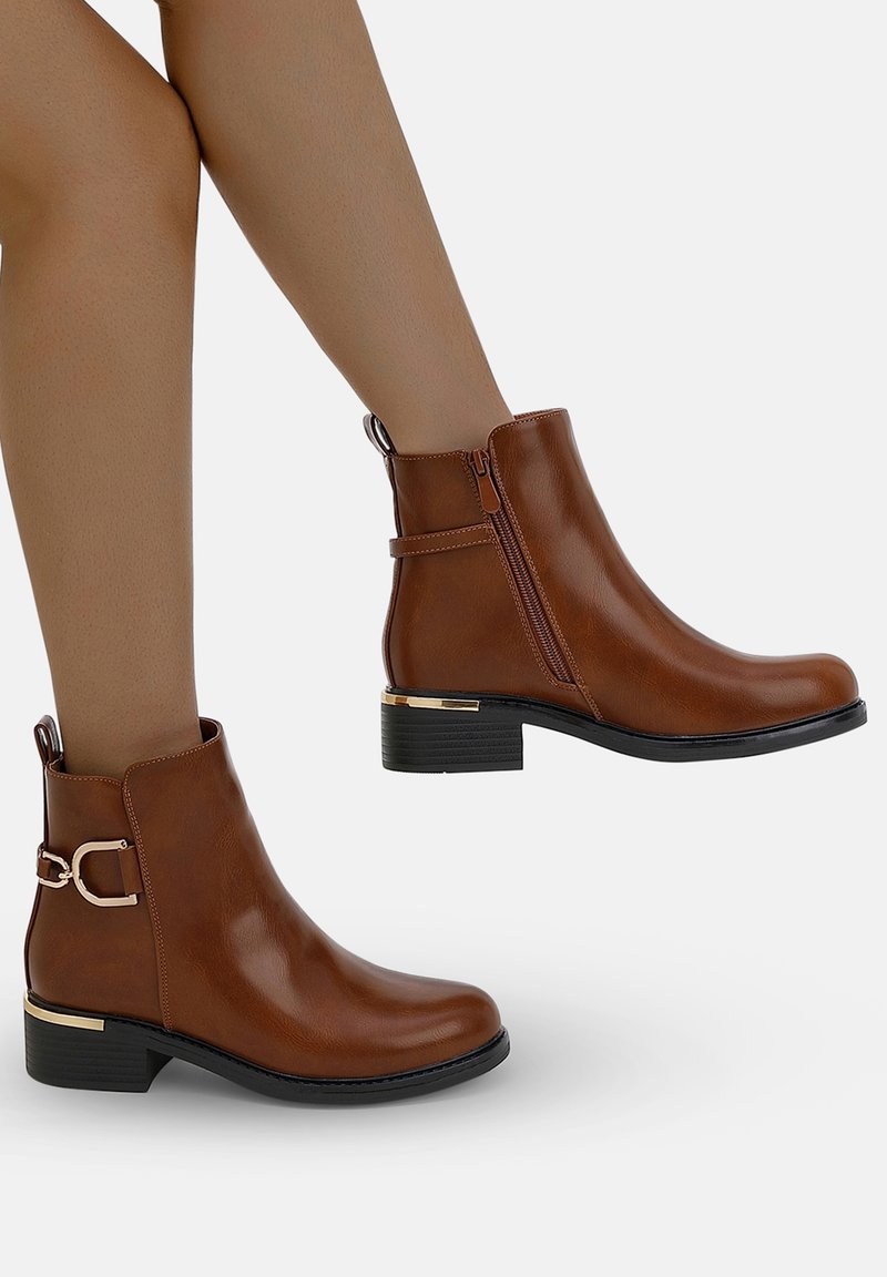 Botas de tobillo marrones hechas de cuero suave, con cremallera lateral, un hebilla decorativa y un tacón bajo con un acento dorado.