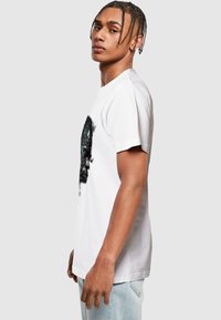 White cotton t-shirt featuring a graphic print in black and teal, crew neckline, short sleeves, and a relaxed fit.