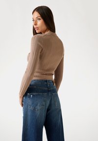 Top beige a costine e aderente abbinato a jeans blu in denim larghi. Presenta maniche lunghe e i jeans hanno un design classico delle tasche con lievi segni di usura.