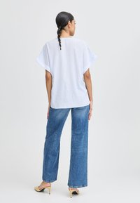 Top oversize blu lichto realizzato in tessuto testurizzato, abbinato a jeans in denim blu a gamba larga. Completano l'outfit tacchi a slip-on lisci.