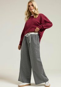 Bordeaux överdimensionerad sweatshirt med långa ärmar, kombinerad med svartvita randiga vida byxor med dragsko i midjan och vita sneakers.