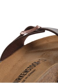 Sandalo in pelle marrone con fibbia in rame, suola testurizzata e cinturino regolabile. Nome del brand "Birkenstock" visibile sulla suola.