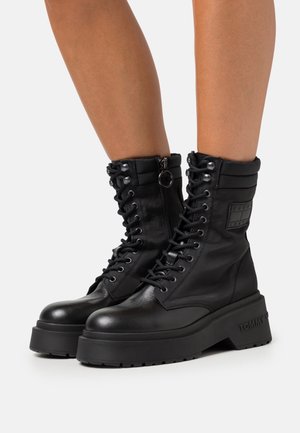 Bottes de combat en cuir noir avec une semelle plateforme épaisse, fermeture à lacets sur le devant, fermeture éclair et accent de marque sur le côté.