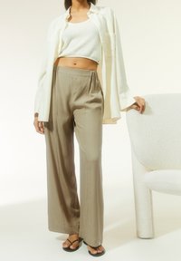 Lehká krémová košile, bílé ribbed crop top, béžové kalhoty širokého střihu a černé žabky, vše na neutrálním pozadí.