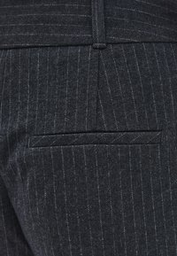 Marineblauwe stof met fijne strepen en een subtiele textuur; voorzien van een achterzak met een gestroomlijnde opening en netjes afgewerkte randen.