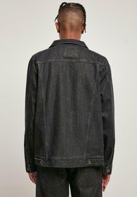 Sorte denimjakke med klassisk krage, synlige sømmer og knappedetaljer. Har rett snitt og en litt teksturert overflate.