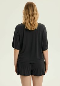 Czarny zestaw odzieży domowej składający się z luźnej koszulki z krótkim rękawem i pasujących szortów, wykonany z miękkiego, lekkiego materiału.