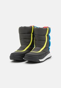 Botas acolchadas negras con costuras amarillas, detalles azules y una suela negra texturizada. Tienen una parte superior redondeada y lengüetas de tirón en rojo y azul.