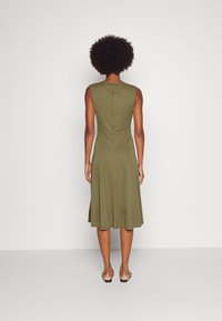 Olivově zelené bezramínkové šaty s přiléhavým korzetem a rozšířenou sukní, vyrobené z hladkého materiálu. Mají zadní zapínání na zip.