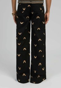 Pantalons larges noirs avec des motifs de feuilles brodés en or et blanc. Dotés d'une taille haute et de deux poches arrière. Texture de tissu douce.