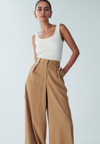 Vitt ribbat linne kombinerat med högmidjade, vida beige byxor med veck fram och sidfickor. Slät textur överallt.