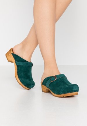 Teal ruskindsklodser med en træsko, der har en rund metalspænde og lukket tå. Enkel design og blød tekstur.