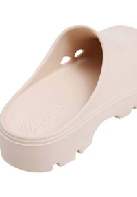 Ljusrosa sko utan snörning gjord av texturerad gummi. Har en slät ovandel med två ventilationshål och en tjock, räfflad sula.