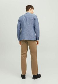 Jasnoniebieska lniana marynarka z jednym rozcięciem, w zestawieniu z beżowymi spodniami i czarnymi butami. Strój charakteryzuje się klasycznym designem i neutralnymi kolorami.