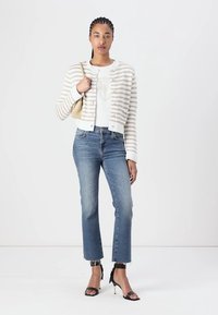 Gestreifter Creme- und Beige-Cardigan über einem weißen Oberteil, kombiniert mit blauen Jeans und schwarzen High Heels; minimalistisches Design, lässiger Stil.
