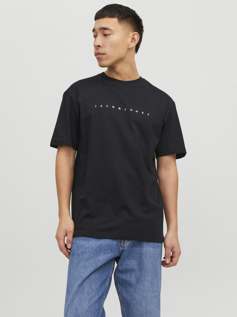 Schwarzes Baumwoll-T-Shirt mit Rundhalsausschnitt, versehen mit dem Markenlogo "JACK & JONES" in der Mitte der Brust. Getragen mit hellblauen Jeans.