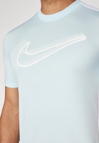 Light blue athletic shirt with short sleeves, made of smooth fabric, featuring a prominent white Nike logo design across the front.