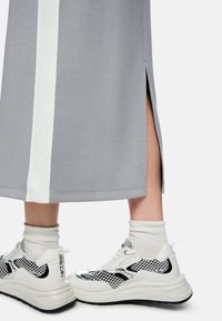 Grauer Sportrock mit weißem Streifen an der Seite und seitlichem Schlitz, kombiniert mit weißen und schwarzen Mesh-Sneakern mit dicken Sohlen.