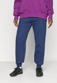 Jogging en bleu marine en tissu doux, avec des jambes effilées, des poches latérales et des poignets côtelés. Associé à des chaussures de sport noires.