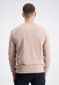 Felpa beige con maniche lunghe, polsini e orlo a costine, texture liscia e una piccola toppa rettangolare sulla parte superiore della schiena.