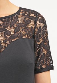 Czarny top z krótkimi rękawami; koronkowe wykończenie z kwiatowymi wzorami na ramionach; gładka tkanina na tułowiu; okrągły dekolt.