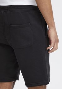 Schwarze Baumwollshorts mit glatter Textur, ausgestattet mit einer Seitentasche, elastischem Bund und gesäumten Bündchen. Einfaches und funktionales Design.