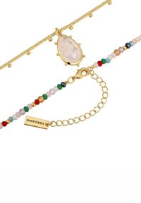 Goldfarbener Armreif mit einem tropfenförmigen, klaren Steinhänger und einer Beaded-Kette mit mehrfarbigen Steinen sowie einem Verschluss.