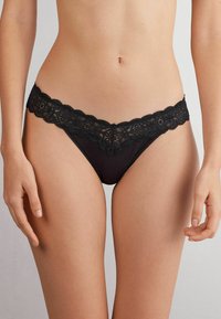 Bikini en dentelle noire avec une bordure festonnée, une taille lisse et un motif floral délicat. Le tissu doux offre un ajustement léger et confortable.