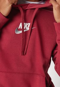 Röd bomullshoodie med en framficka i kängurustil, dragsnören och en vit Nike-logotyp tryckt på bröstet.