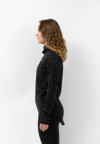 Schwarzer Leopardenmuster-Vollzip-Pullover mit hohem Kragen, langen Ärmeln und Daumenlöchern, getragen mit passenden Leggings, die eine weiche Textur aufweisen.