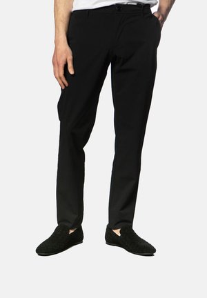 Black tailored trousers in lightweight fabric, featuring a straight-leg design and side pockets, paired with textured black slip-on shoes.