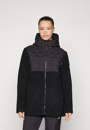 Sort jakke med mock neck, med et quiltet toppseksjon og teksturerte fleece-ermer. Glidelås, avslappet passform, og uten synlige logoer.