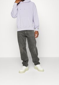 Light purple hooded sweatshirt with a kangaroo pocket, paired with gray jeans and white chunky sneakers. The sweatshirt has a subtle logo.