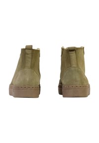 Botas de tobillo de ante verde oliva con punta redonda, forro suave y suela de goma beige. Cuenta con una tira en la parte posterior para facilitar el uso.