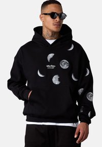 Sweatshirt à capuche noir avec des graphismes de lune blanche et une poche avant. Fabriqué en tissu doux avec un ourlet et des poignets côtelés.