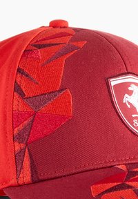 Czerwona czapka baseballowa z teksturowanym, geometrycznym wzorem, solidnym szczytem, zakrzywionym daszkiem oraz naszywką w kształcie tarczy z przodu.