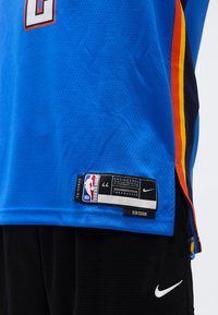 Maillot de basketball NBA swingman bleu avec étiquette taille 44 et logo Nike, porté avec un short de sport noir Nike.