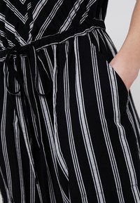 Combinaison à rayures noir et blanc avec une taille cintrée à nouer, des poches et un tissu texturé pour plus de confort.