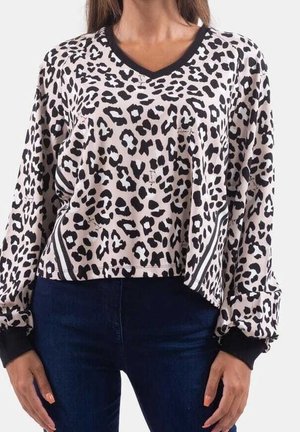 Femme portant un haut beige à manches longues imprimé léopard avec des poignets noirs et un col en V noir, assorti à un jean bleu foncé.