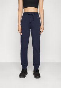 Marineblaue Baumwoll-Jogginghosen mit Kordelzugbund, schmal zulaufenden Beinen und seitlichen Taschen, kombiniert mit schwarzen Sportschuhen.