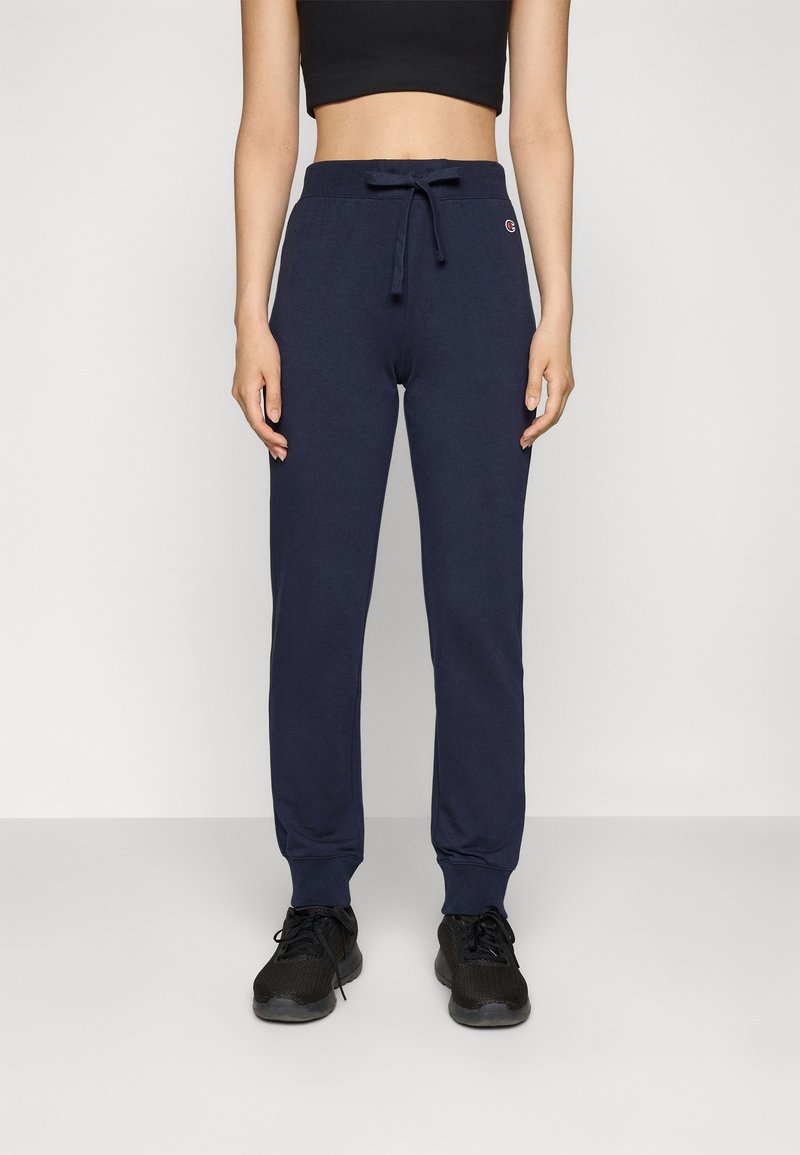 Marineblaue Baumwoll-Jogginghosen mit Kordelzugbund, schmal zulaufenden Beinen und seitlichen Taschen, kombiniert mit schwarzen Sportschuhen.