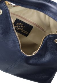Marineblauwe leren handtas met een diepe textuur en gouden rits. Het interieur heeft een beige voering en een label met de tekst "Gemaakt in Italië."