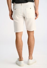Bermuda bianche in cotone con una finitura testurizzata, dotate di tasche posteriori e un taglio dritto. Indossate con sneakers bianche.