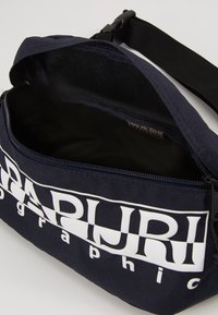 Borsa a vita blu navy con spallaccio nero regolabile, zip aperta e grande logo bianco "Napapijri geographic" sul fronte.