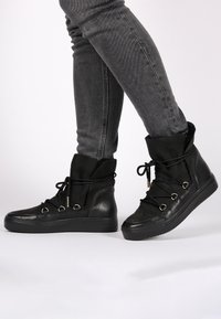 Botines negros de cuero y ante, con punta redonda, cordones frontales y ojales metálicos, con una suela de goma texturizada.