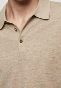 Polo beige en lin avec un col, comportant deux boutons marron et un tissu tissé texturé.