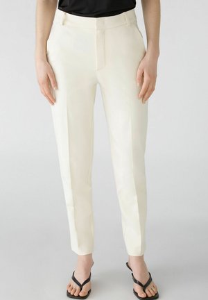 Cream-colored tailored trousers with a smooth texture, flat front, and tapered legs, paired with black flip-flops.
