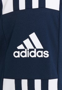 Tejido de color azul marino con un acabado texturizado presenta un gran logotipo blanco de Adidas y tres franjas blancas a lo largo del área de los hombros.