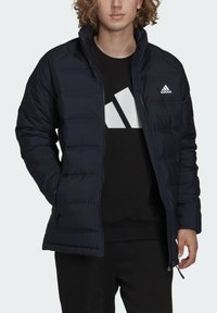 Giacca a vento blu navy con design trapuntato, colletto alto e chiusura con zip, indossata sopra una felpa nera con un logo bianco.